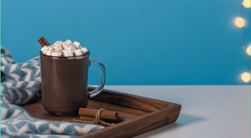Cozy Fleece Blanket Scene Photograph of a steaming mug of hot chocolate with marshmallows and cinnamon on a wooden tray, set against a cozy, festive background with a patterned blanket and bokeh lights.