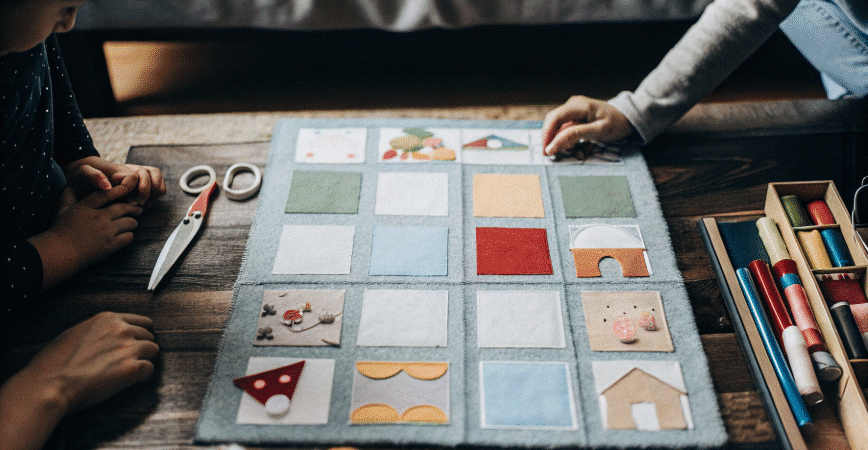 Photograph of a vibrant felt activity board surrounded by colorful craft supplies on a wooden table, highlighting creativity and hands-on learning.