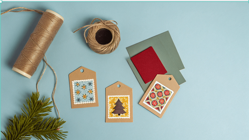 DIY Gift Tags Flat Lay Photograph showcasing various handcrafted Christmas gift tags with festive stamps, surrounded by crafting supplies like twine, ink, and pine branches on a dark background.