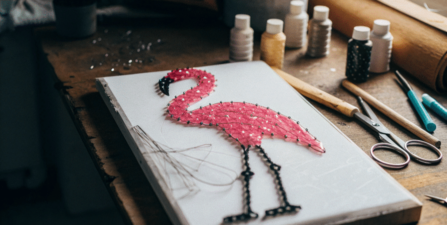 Flamingo Nail Art DIY Photograph of a vibrant pink and black flamingo string art on a white board, surrounded by crafting tools, conveying creativity and DIY charm.