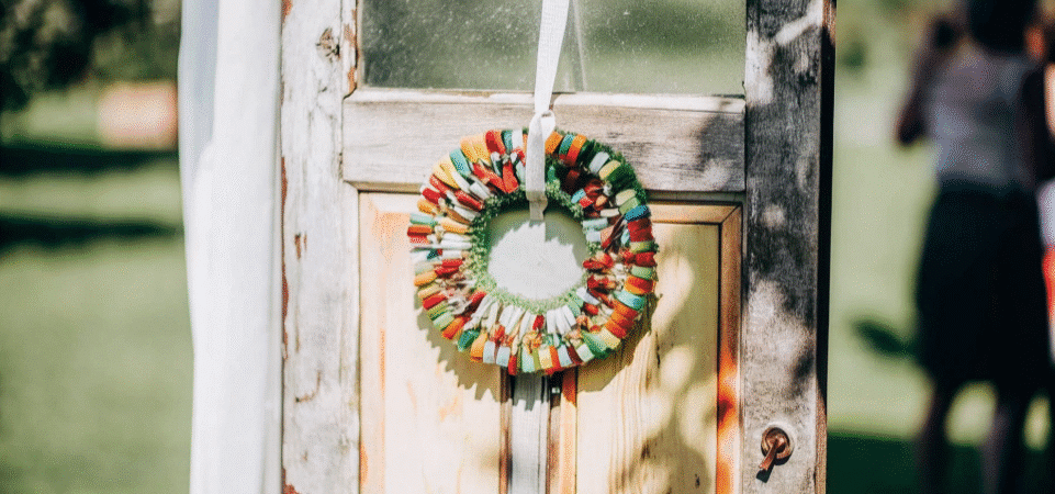 Photograph of a vibrant, handmade wreath crafted from colorful paper and recycled bottle caps, hanging on a rustic wooden door, evoking creativity and sustainability.