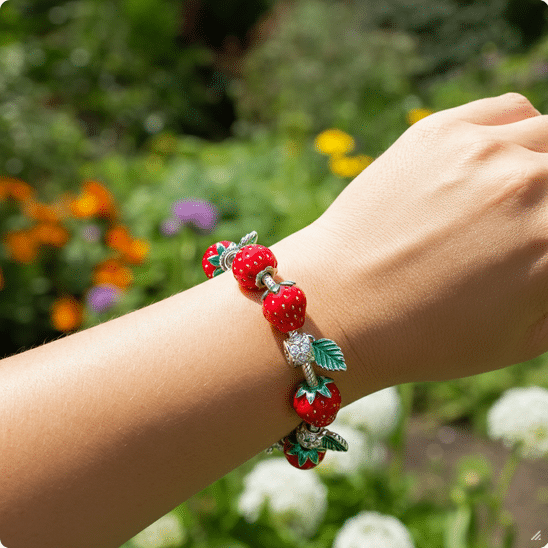 Strawberry Bracelet Lifestyle Photograph of a woman's arm wearing a vibrant strawberry charm bracelet, set against a soft-focus garden background, evoking summer joy and natural elegance.