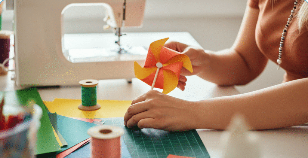 Tips for a Successful Crafting Session Photograph of a person's hands crafting a vibrant paper pinwheel on a bright table surrounded by colorful craft supplies and a sewing machine, evoking creativity and DIY spirit.