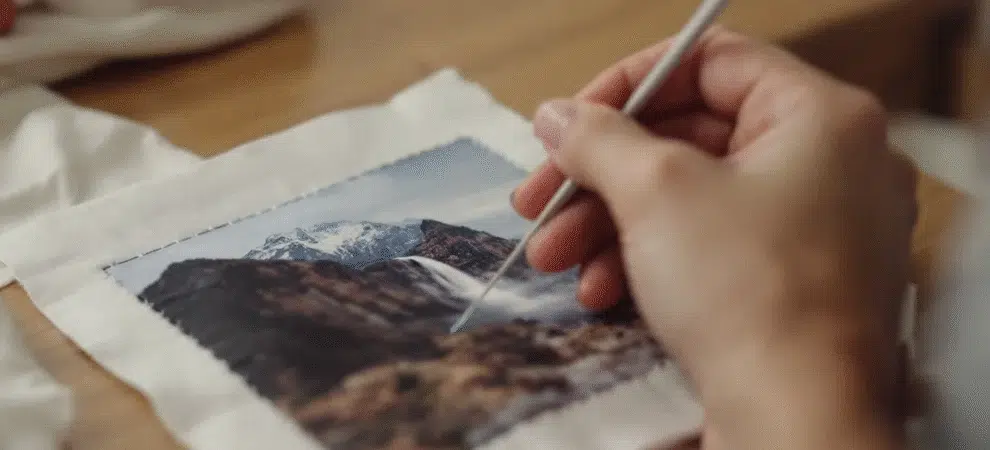 The image features a vibrant display of various appliqué patterns and techniques, showcasing a light box with a photo being transformed into a decorative fabric piece. Surrounding materials include colorful background fabric and stitched shapes, illustrating the fun and creativity involved in turning a picture into an appliqué for clothing or quilts.