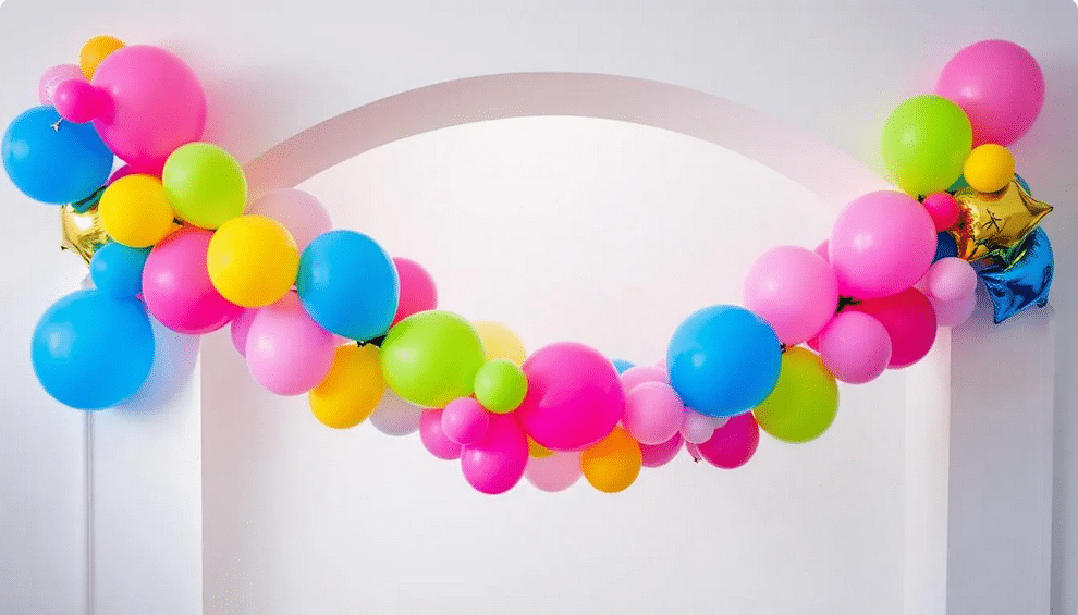 The image features a vibrant pink balloon garland elegantly draped along a wall, creating a festive backdrop perfect for a birthday party or baby shower. The garland includes a mix of balloon sizes and colors, adding a fun and dynamic touch to the party decorations.