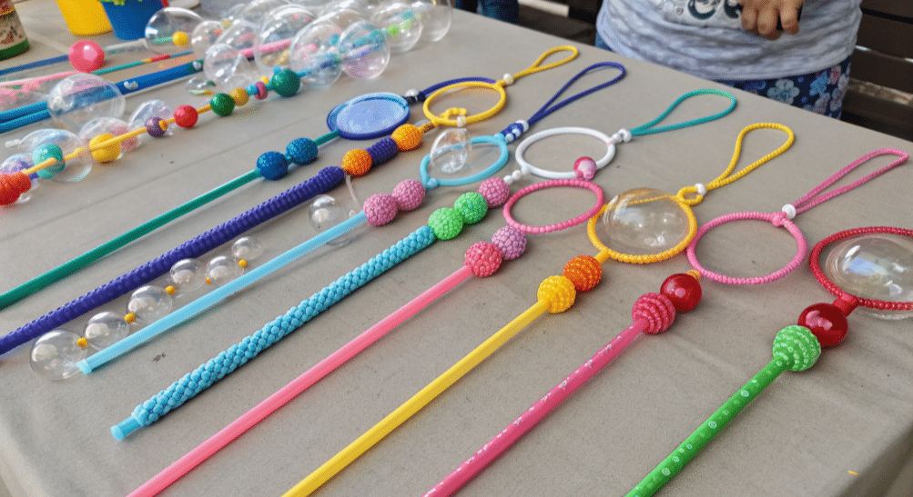 A colorful assortment of DIY bubble wands made from straws, cotton string, and beads is displayed on a table, inviting creativity and fun. The image showcases various shapes and sizes of bubble wands, perfect for kids' parties or family gatherings, ready to create big bubbles and joyful moments.