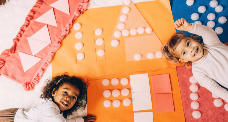 The image showcases preschoolers engaging in a fun math craft activity, using colorful construction paper and pom poms to practice counting and number recognition. The children are happily creating shapes and numbers, fostering their fine motor skills and creativity in a lively learning environment.