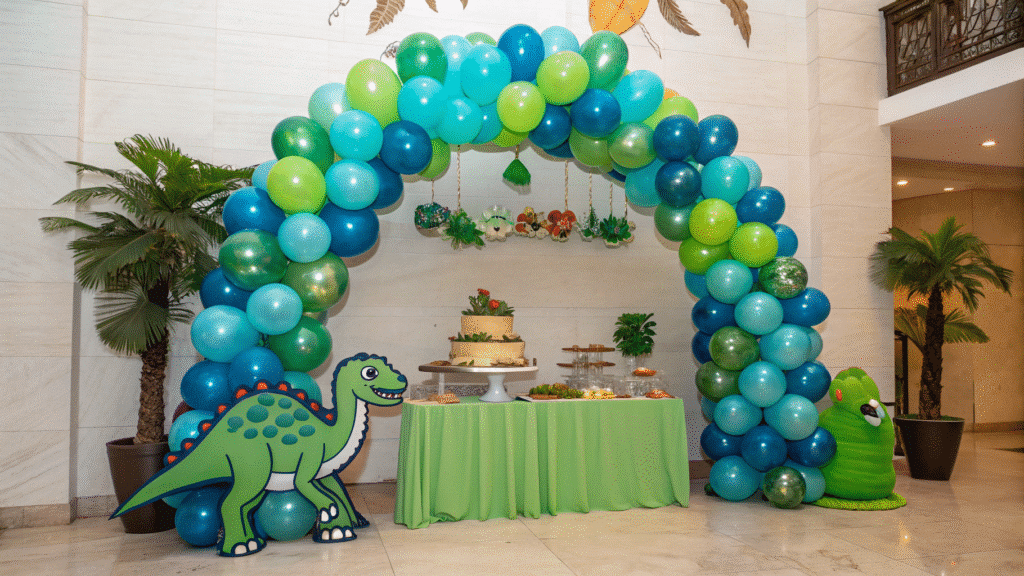 The image features a vibrant dinosaur-themed party setup, complete with a colorful dinosaur balloon arch made of green and blue foil balloons. Surrounding the arch are matching centerpieces that enhance the festive atmosphere, perfect for a kids' birthday party or baby shower.