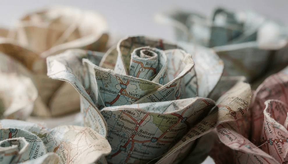 A close-up photograph showcases stunning handmade paper roses, intricately crafted with map details that reveal city names and roads on their curved petals. These unique map roses, perfect for home decor or gifts, blend art and creativity, offering a fresh take on traditional flower arrangements.