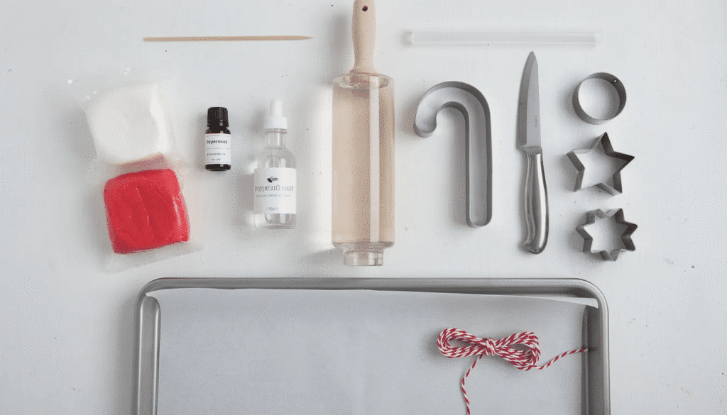 An assortment of supplies for making DIY candy cane ornaments is displayed, including white and red polymer clay, peppermint essential oil, a small rolling pin, cookie cutters, and twine for hanging. This setup is perfect for creating homemade Christmas ornaments that can be enjoyed with family and friends.