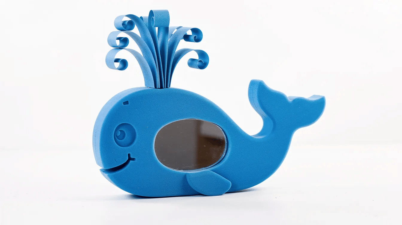 74d5cbaf-8c16-4799-a365-089cb5bb8353 A bright blue whale-shaped craft mirror made from foam features a small oval mirror as the whale's belly, with curled paper forming a whimsical water spout on top. This beautiful animal-themed mirror is perfect for kids' rooms or playful home decor.