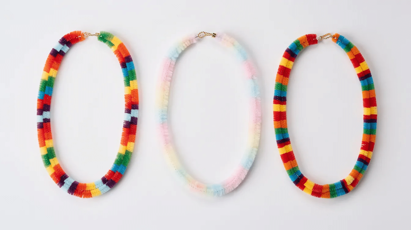 a62a2135-1c4d-4dbb-9a0d-01579216684c The image features three finished pipe cleaner necklaces, each showcasing unique color patterns, laid flat on a white surface. These colorful creations, made with pipe cleaners and beads, highlight the fun and creativity of crafting jewelry for kids.